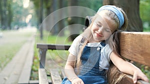 Small tired child girl sitting on a bench with closed eyes resting in summer park