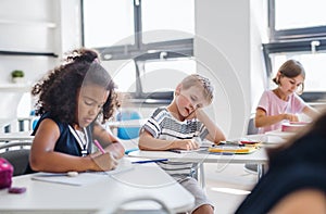 A small tired school boy sitting at the desk in classroom, sleeping.