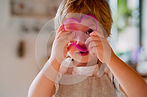 A small toddler boy looking through a cake cutter at home.