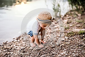 A small toddler boy standing outdoors by a river in summer, playing.