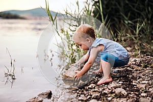 A small toddler girl playing outdoors by the river in summer.