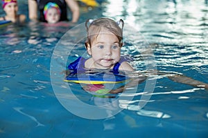 Small toddler kid learns to swim with board in pool. Swimming lesson. Active kid plays in water