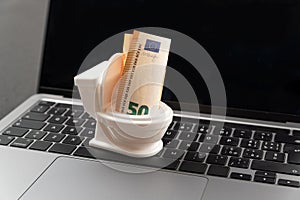 Small toilet with euro cash inside, is on laptop keyboard. Concept of lost money or rash purchases