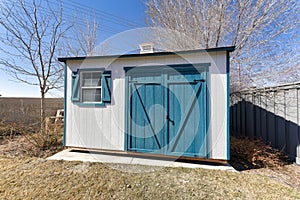 Small tool shed exterior with white wooden wall and blue green double doors and window shutters