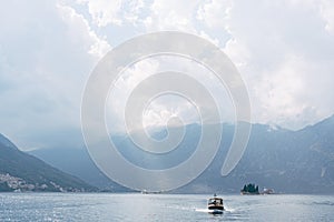 A small tourist boat sails on the Bay of Kotor with the islands in the background near Perast in Montenegro, against the