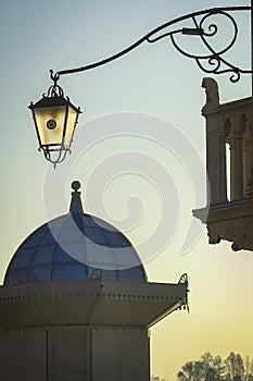 A small tower and a fishnet lantern shine through in the sun, against the backdrop of a blue sunset sky