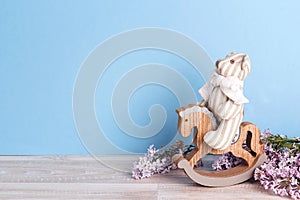 A small toy bear on a rocking horse with lilac flowers on a blue background