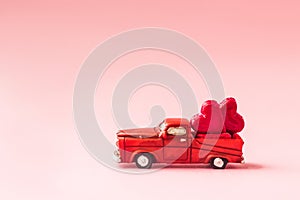 A small toy car carries candy in the shape of hearts on a pink background. Valentine`s day concept. greeting card.Love.selective