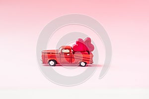 A small toy car carries candy in the shape of hearts on a pink background. Valentine`s day concept. greeting card.Love.selective