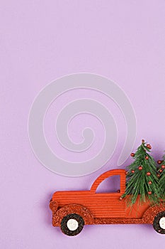Small toy car carring christmas tree on violet background . Sesonal holidays, greeting card, christmas mood concept