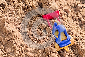 Small toy digger working on sand quarry, construction concept