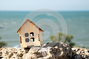 Small toy house on the rock with a blue sea on the background