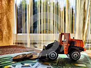 A small toy tractor or excavator on a bundle of money. The concept of the high cost of technology. The possibility of