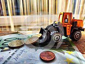 A small toy tractor or excavator on a bundle of money. The concept of the high cost of technology. The possibility of