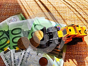 A small toy tractor or excavator on a bundle of money. The concept of the high cost of technology. The possibility of