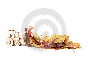 Small toy tractor is loaded with yellow fallen leaves against a white. Cleaning and removal of fallen leaves