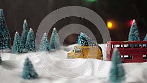 A small toy yellow toy car with a Christmas tree on the roof fast rides through a miniature toy forest with snowdrifts
