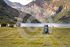 Small tractor with round baler haymaking on a field in Geiranger, Norway