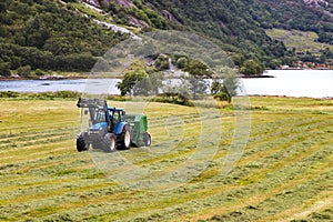Small tractor with round baler haymaking on a field in Geiranger, Norway
