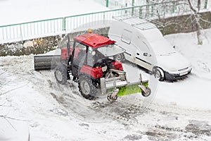 Small tractor snow plow in courtyard during work in snowfall