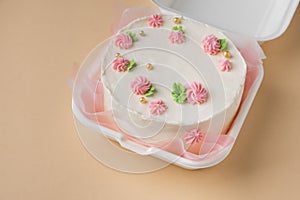 Small traditional Korean style bento cake with white cream cheese frosting decorated with pink whipped cream flowers. Little