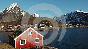 Small traditional Scandinavian village with red houses on the picturesque fjord coast. Beautiful mountains covered white