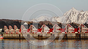 Small traditional Scandinavian village with red houses on the picturesque fjord coast. Beautiful mountains covered white