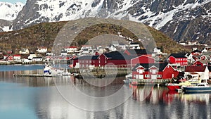 Small traditional Scandinavian village with red houses on the picturesque fjord coast. Beautiful mountains covered white