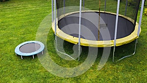 Small trampoline near big one with round mat, size comparison, green lawn background