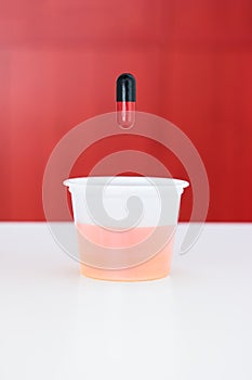 Small transparent plastic medicine drinking cup with red and black medicament capsule above it shallow depth of field