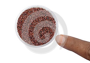 A small tray filled with tiny red Garnet minerals, a finger is pointing to it