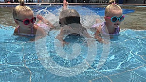 small triplets sisters playing in the pool in swimsuits