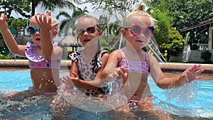 small triplets sisters playing in the pool in swimsuits