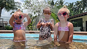 small triplets sisters playing in the pool in swimsuits