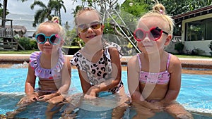 small triplets sisters playing in the pool in swimsuits