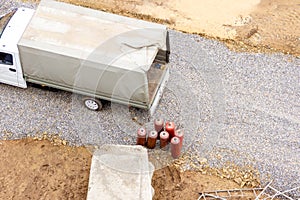 A small truck with an awning on the body stands on a construction site near several red gas cylinders - propane