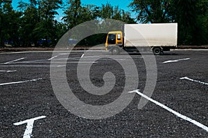 Small truck with a yellow cab and a white one-trailer in a parking lot with direction arrows