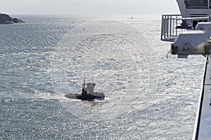 Small Tug boat saling on shining sunny sea viewed from a big cruise ship desk photo