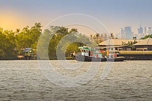Small tugboat is pulling a large shipping barge up the Chao Phraya River in Bangkok, Thailand.