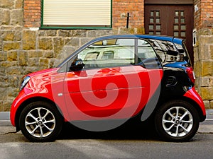 Small two-seater red and black modern compact town car in side view in old urban setting