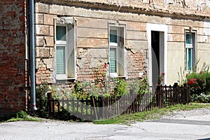 Small urban garden in front of old red brick suburban family house with dilapidated cracked facade surrounded with brown picket