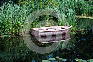 Small vessel reflecting in a creek with green water reeds, Barendrecht, The Netherlands