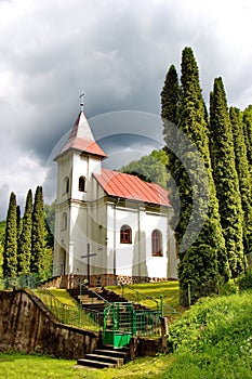 Malý dedinský kostol obklopený stromami s oblakmi na pozadí