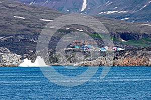Small village with colorful wooden houses and iceberg in front in the back of beyond on Arctic Ocean near Qeqertarsuaq, Greenland
