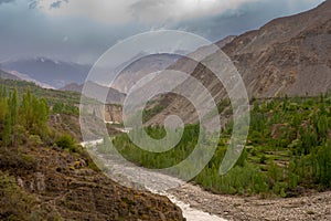 A small village lying in a rocky valley underlying blue cloudy sky with green pine trees and rice field