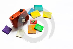 A small vintage camera of brown color is made of plasticine. Next to the camera is a few photos of bright and colorful flowers.