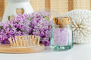 Small vintage glass bottle with purple bath salts epsom salt, foot soak, wooden hair brush and lilac flowers.