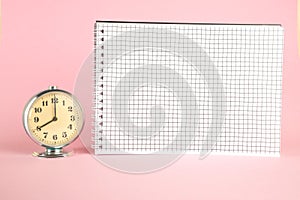 Small vintage retro alarm clock and notebook on pink isolated background