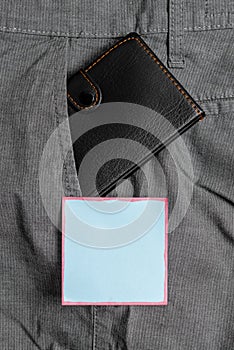 Small wallet in the trousers front pocket beside blue note sheet. Little purse is placed inside man pants near notation