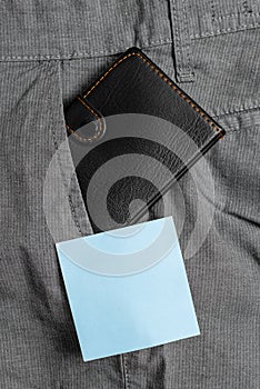 Small wallet in the trousers front pocket beside blue note sheet. Little purse is placed inside man pants near notation